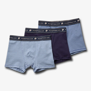 Drie jongensboxers liggen naast elkaar, één gestreept en twee effen. Elk heeft een elastische tailleband met de tekst "POMPdeLUX" erop, tegen een witte achtergrond.