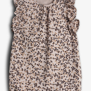 Een babyrompertje met ruches aan de schouders, bedrukt met een patroon van bruine en beige bloemen, hangt tegen een lichte achtergrond. Tekst bovenin: "PMP.CILK ORGANIC COTTON".