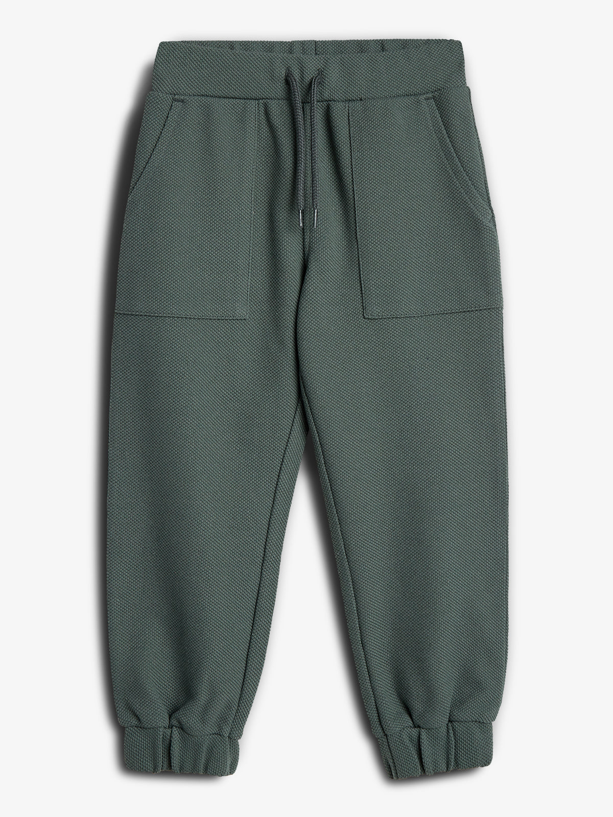 Een groene joggingsbroek met elastische tailleband en trekkoord, heeft twee voorzakken en elastische boorden, afgebeeld tegen een witte achtergrond.