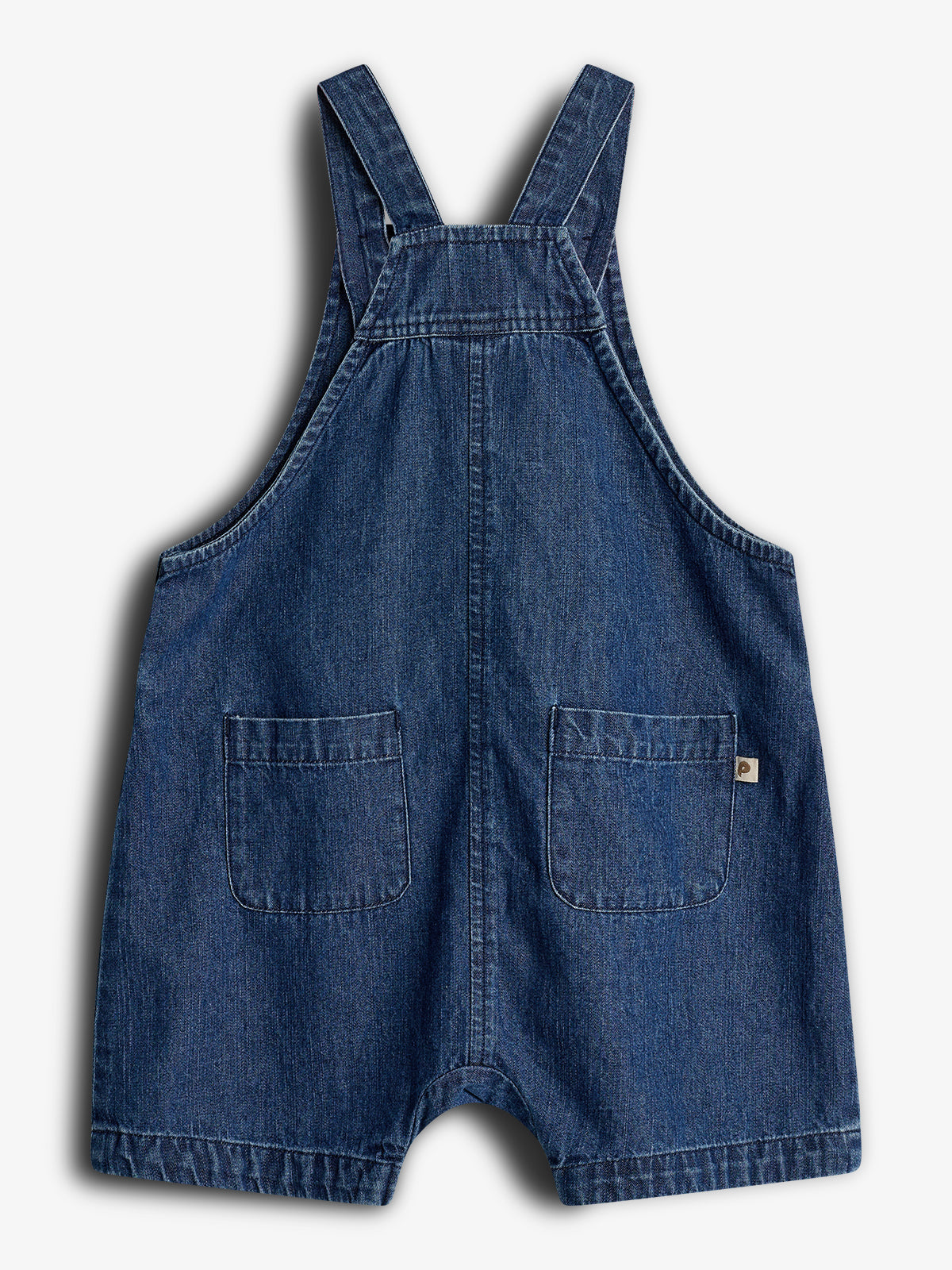 Een donkerblauw denim tuinbroekje hangt rechtop. Het heeft schouderbanden en twee vierkante voorzakken, geschikt voor kinderen. De achtergrond is wit en egaal.
