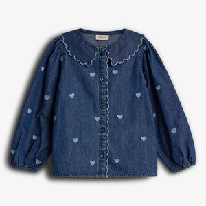 Blauw, denim meisjesblouse met lange mouwen, versierd met kleine hartjes en een geschulpte kraag. De blouse heeft knopen in het midden en een witte achtergrond.