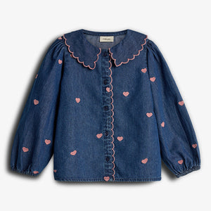Denimblouse met roze hartjespatroon en geschulpte kraag, knopenrij in het midden. De blouse heeft lange pofmouwen en bevindt zich tegen een effen, lichte achtergrond. Label zonder tekst zichtbaar aan de binnenkant van de kraag.