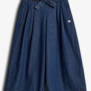 Een blauwe denim culotte met een strikriem en elastische tailleband, symmetrisch gelegen in een neutrale, witte achtergrond. Er is een klein, vierkant label aan de rechterkant.