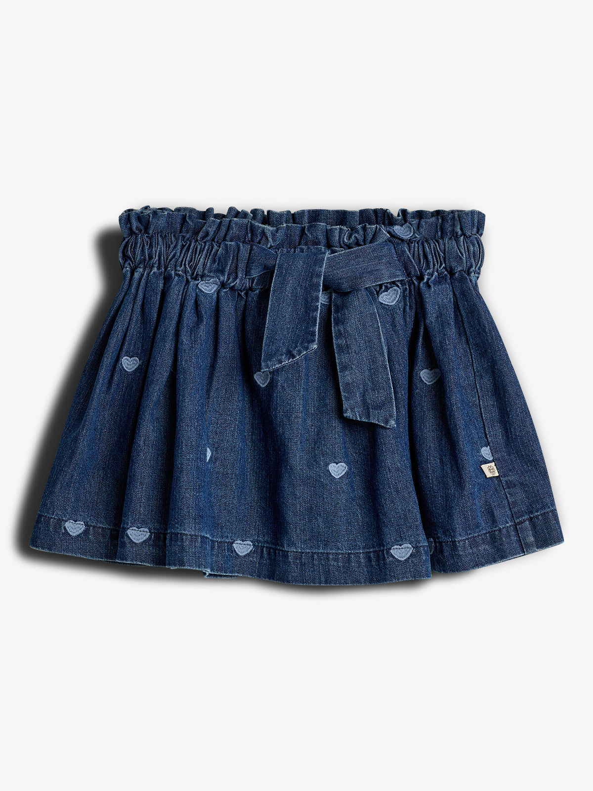 Een blauwe denim rok met elastische tailleband en strik, versierd met kleine geborduurde hartjes, ligt tegen een witte achtergrond.