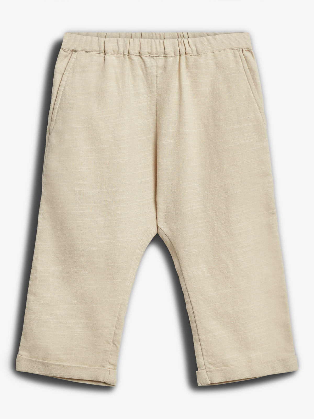 Beige kinderlangebroek met elastische taille en opgerolde broekspijpen, liggend op een witte achtergrond.