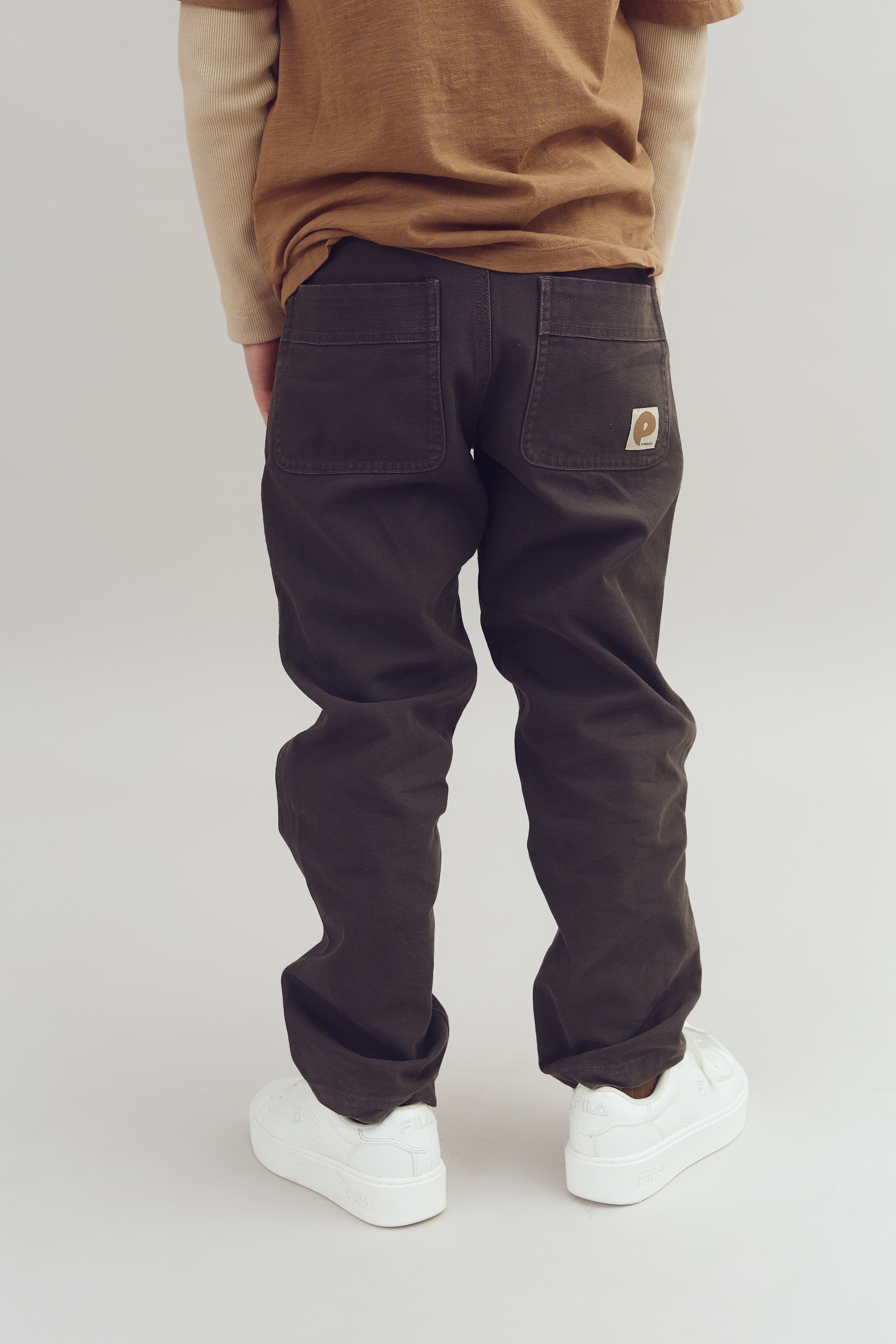 A person stands wearing dark pants with two back pockets and white sneakers marked "FILA," against a plain background.