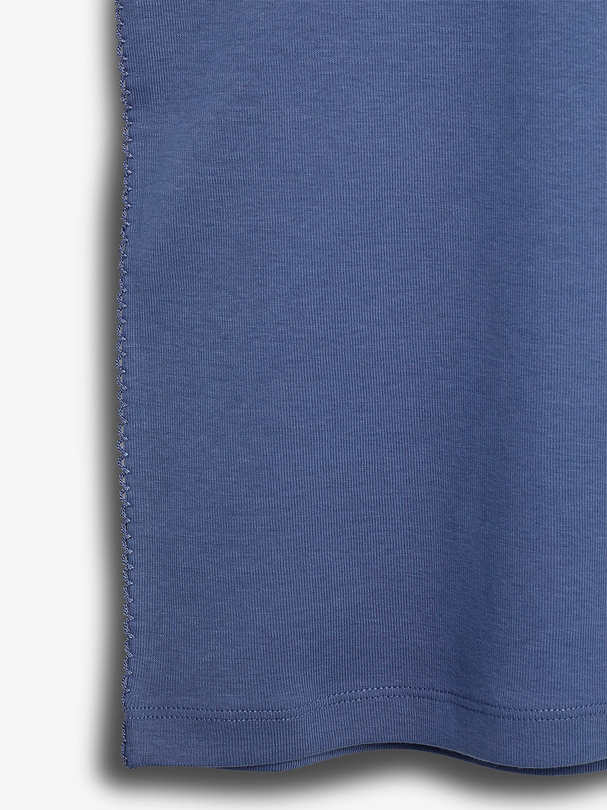 A close-up of blue fabric featuring a visible seam on the left side, showcasing stitch detail. The fabric appears to be part of a garment, like a t-shirt, against a plain background.