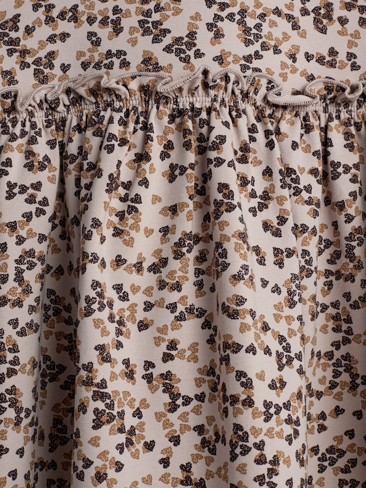 Fabric with a delicate floral pattern in black and beige gathers at a seam, creating a textured, ruffled effect. The background is a neutral off-white.