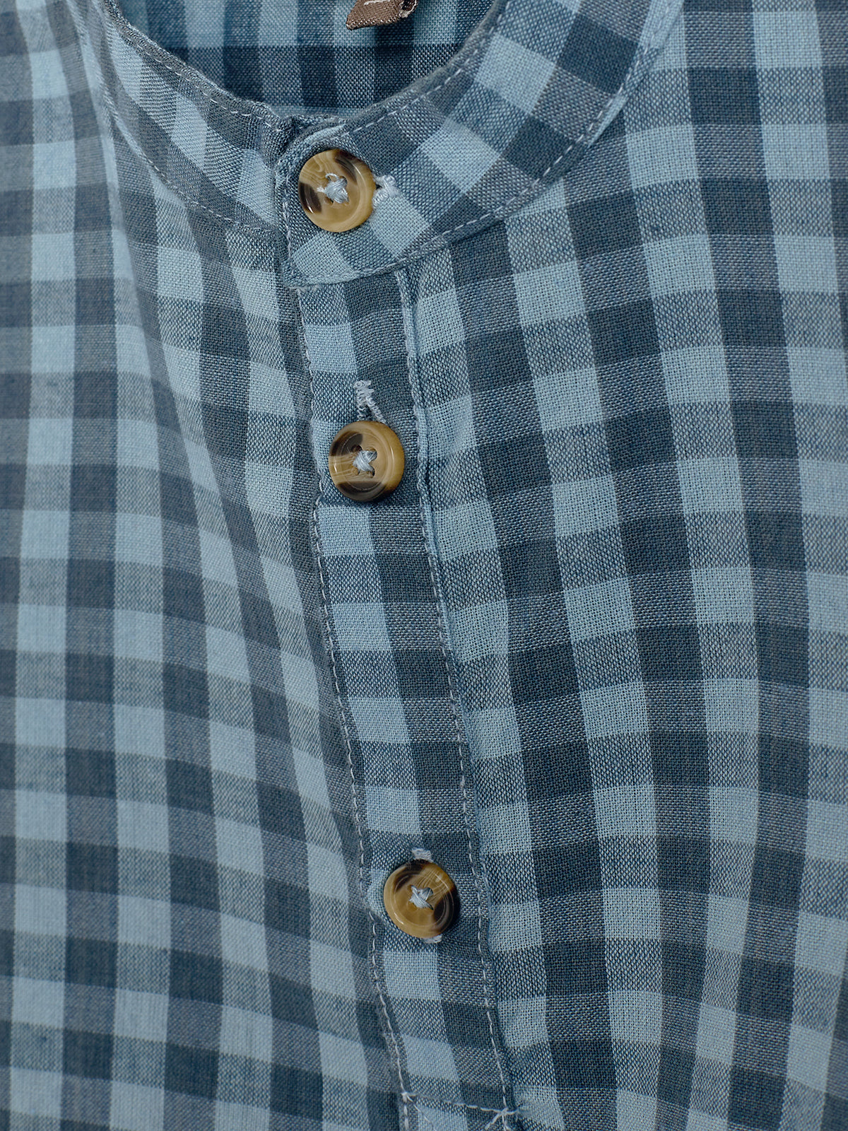 Blauw geruit hemd met drie bruine knopen aan de voorkant, tegen een neutrale achtergrond.