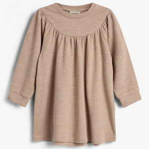 Beige jurk met lange mouwen hangt; eenvoudige, wijde snit met subtiele plooien bij de hals. Witte achtergrond, label met 'mini a ture' zichtbaar aan binnenkant.