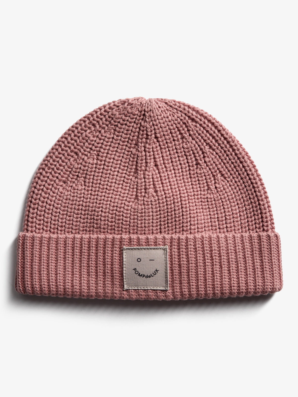 A pink, ribbed knit beanie with a folded brim features a small square patch displaying a simple face and the text "POMPdeLUX" against a plain white background.