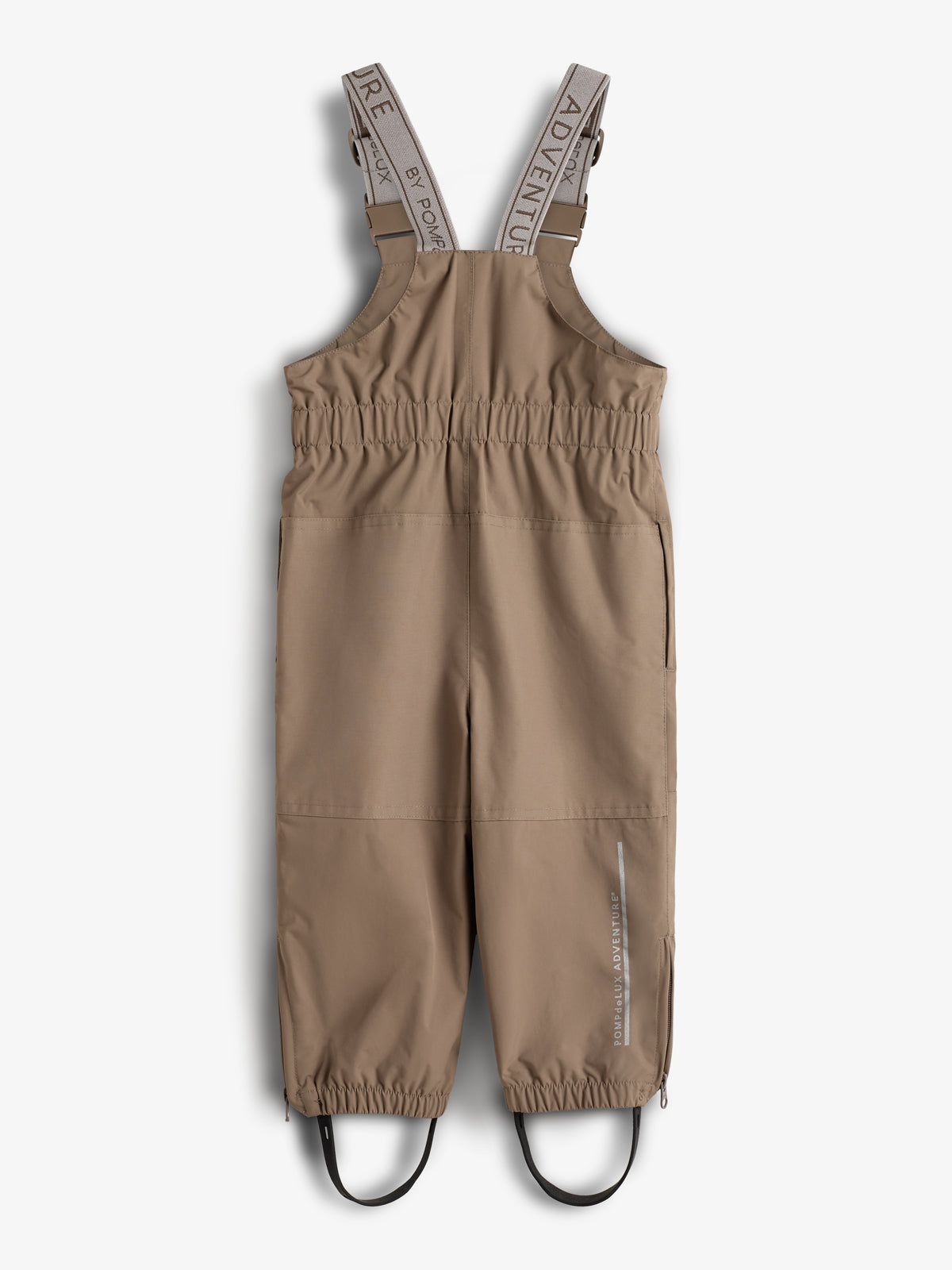 Een bruine kinderbroek met bretels en elastische taille ligt plat. De bretels hebben de tekst "ADVENTURE BY POMPKLADAV". De broek heeft elastieken bij de enkels en voetriemen.