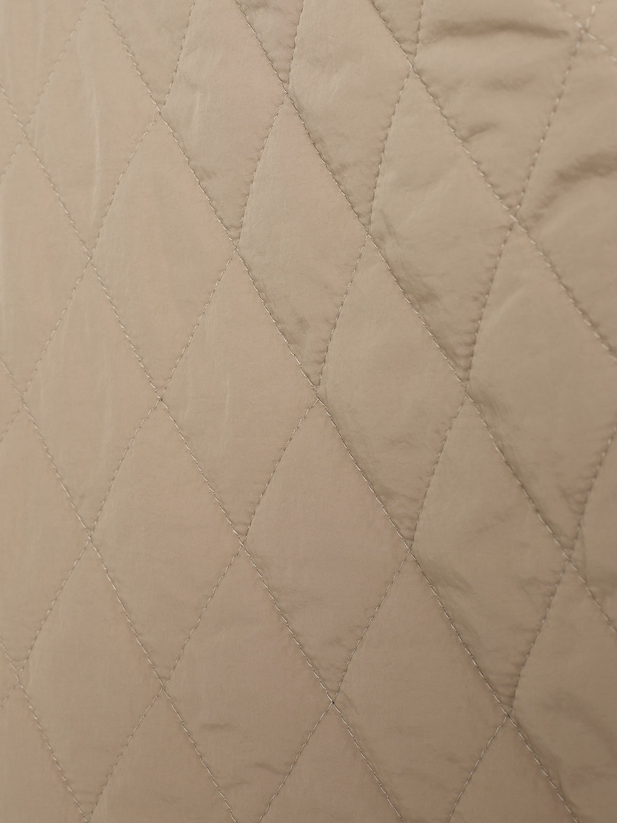 Beige quilted fabric with diamond-shaped stitching creates a textured pattern, filling the entire frame. The fabric appears soft and slightly wrinkled, enhancing its tactile appearance.