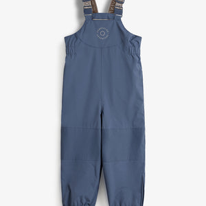Blauwe kinderregenbroek met verstelbare schouderbanden en elastische boorden, tegen een witte achtergrond. Tekst op borst: "COMPLETE LUX ADVENTURE." Bandjes met tekst: "BY POMME" en "ADVENTURE."