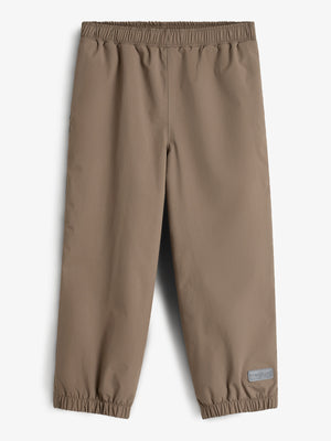 Een bruine regenbroek met elastische tailleband en enkels ligt plat. In de context van een lichte achtergrond. Rechtsonder is een grijs label te zien met de tekst: "Polarn O. Pyret."