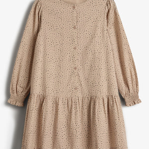 Beige jurk met lange mouwen, bedekt met zwarte stippen en knopen aan de voorkant. De jurk heeft een geplooide zoom en is gefotografeerd tegen een witte achtergrond.